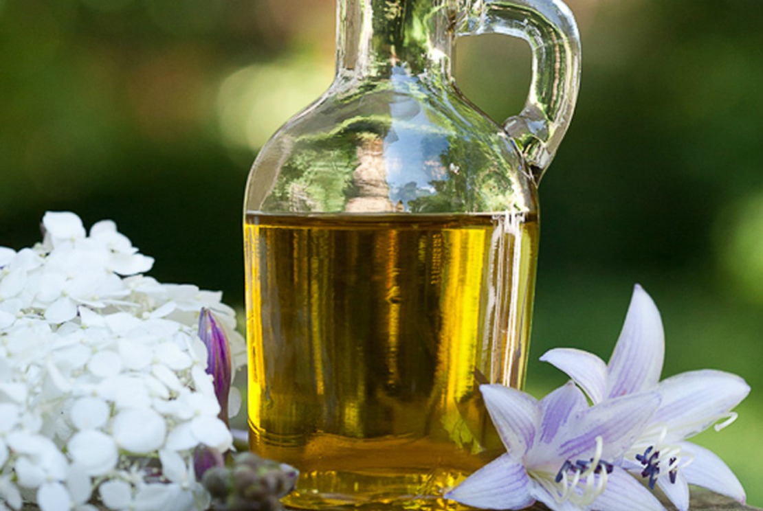 jar of oil with fresh flowers around it