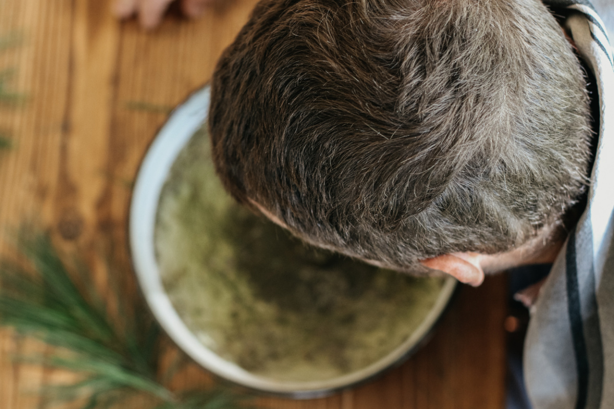 man holding head over herbal steam bowl