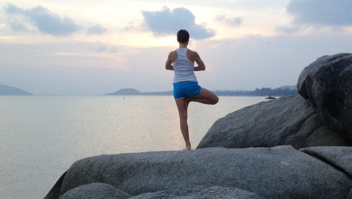 woman doing a yoga pose on a large rock overlooking water