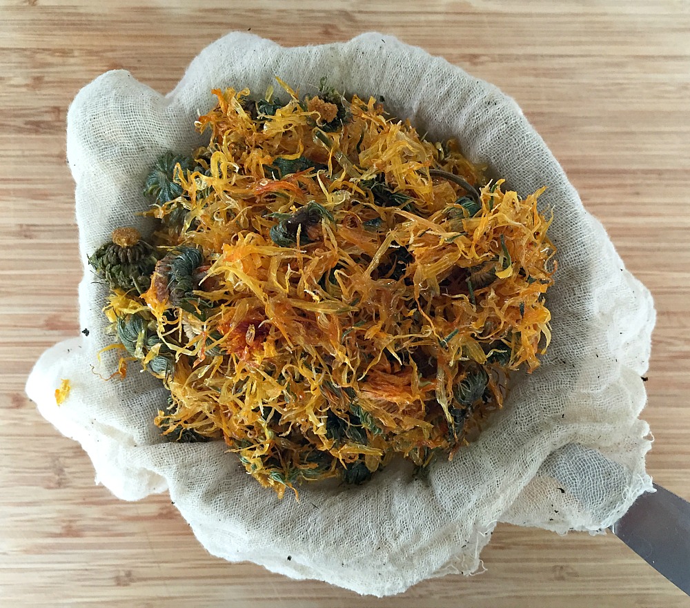 straining calendula through cheesecloth into a bowl