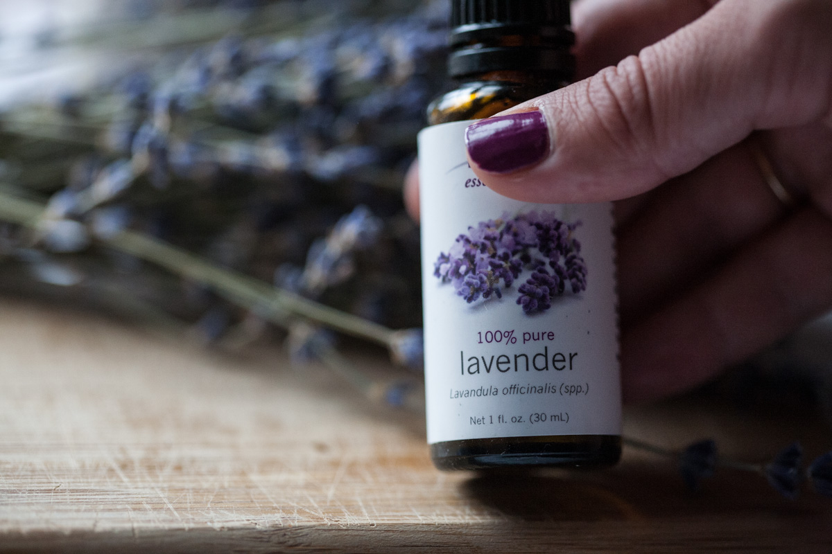 hand holding lavender essential oil with lavender flowers in the background
