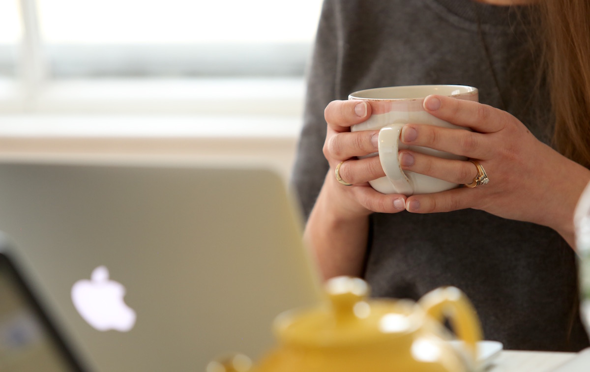 woman holding a cup of tea while looking at a laptop