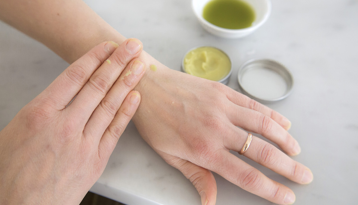 hand rubbing salve on arm with bowl and tin of salve in background