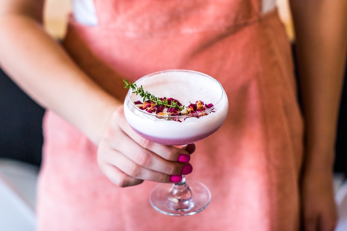 holding pink drink with roses and rosemary