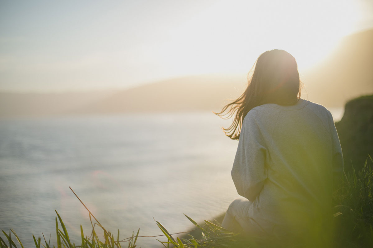 woman sitting on the grass looking at the ocean