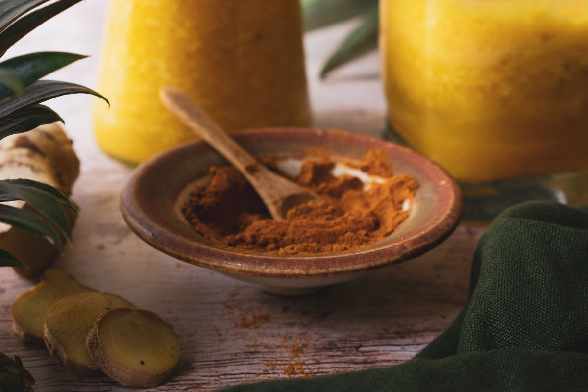 A bowl of turmeric powder with smoothies behind it on table