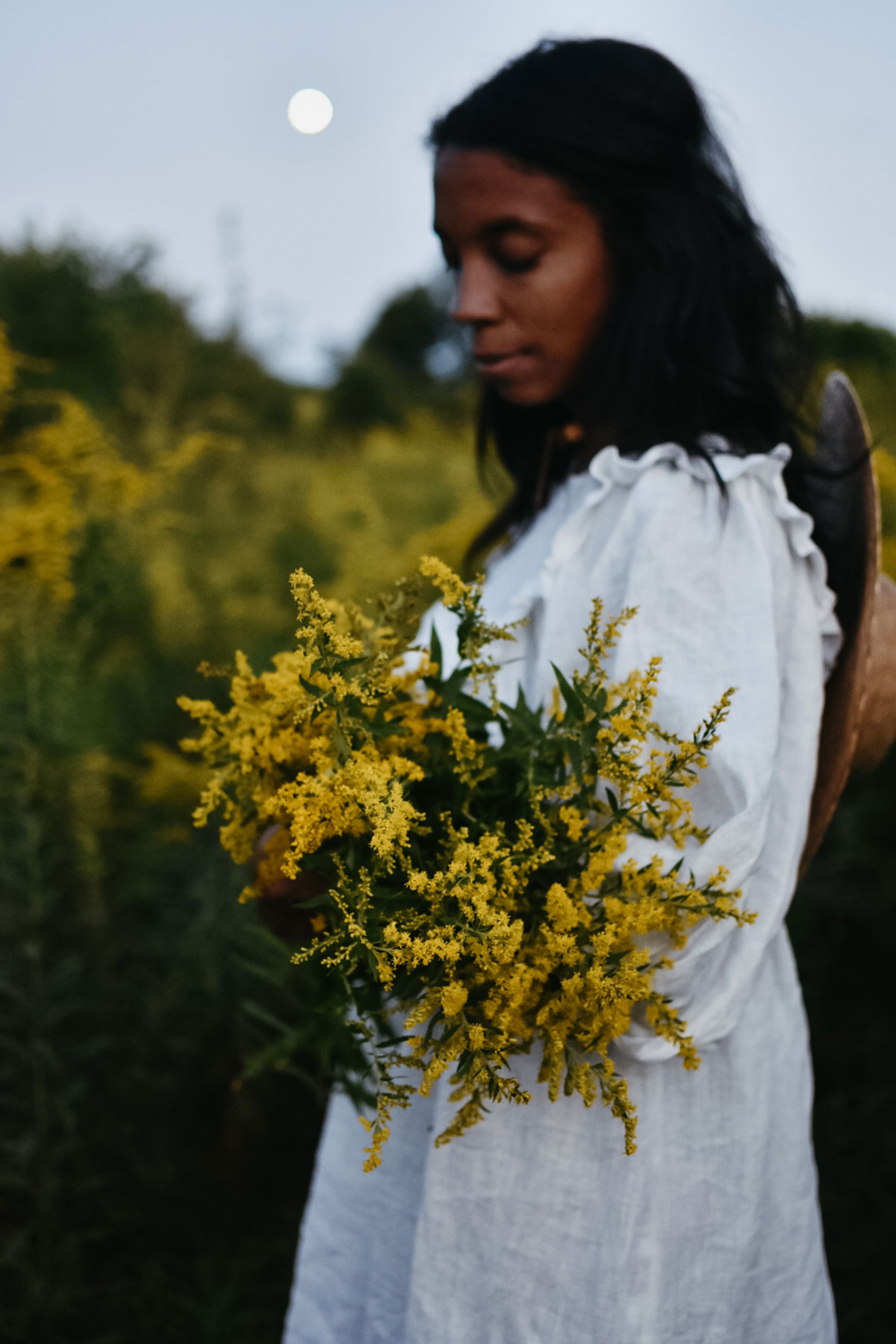 Alyson Morgan holding goldenrod in a field with the moon behind her