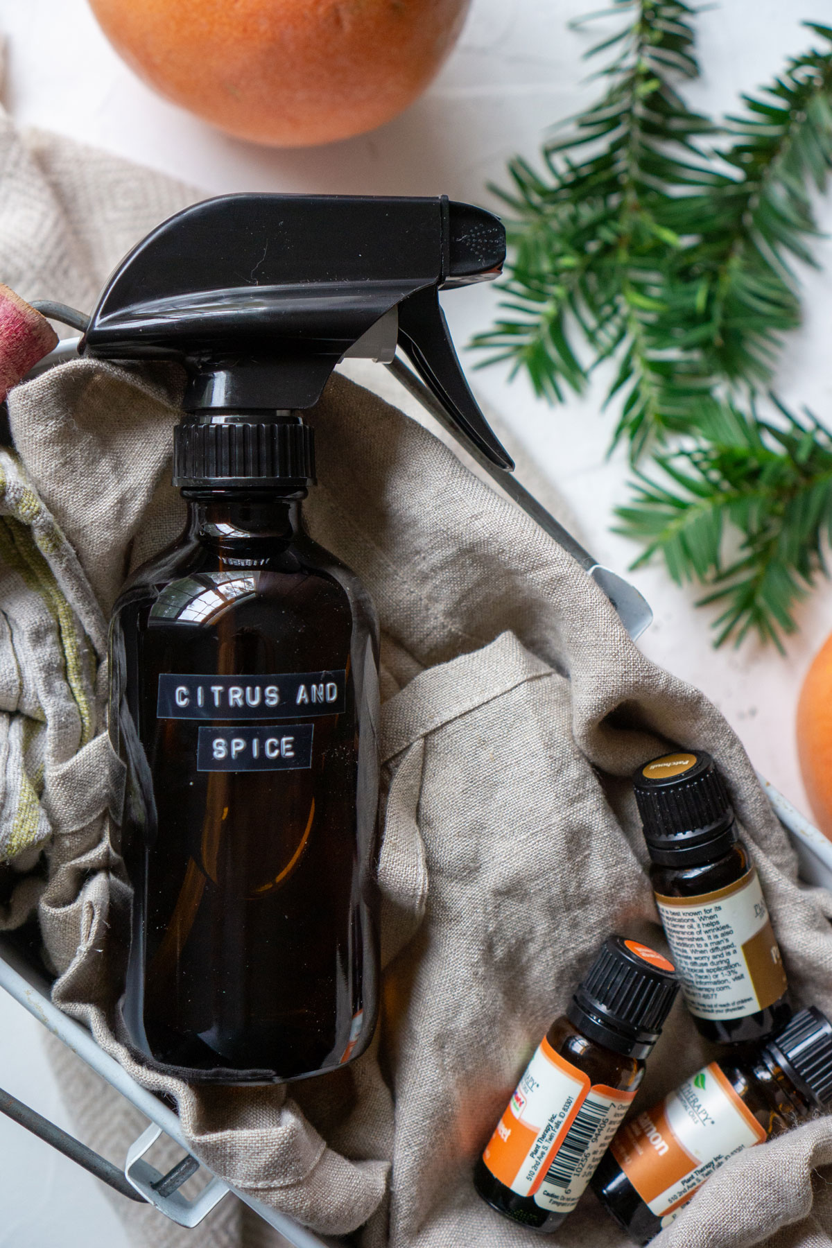 Citrus and Spice cleaner in an amber jar surrouned by grapefruits, essential oils, and evergreen sprigs. 