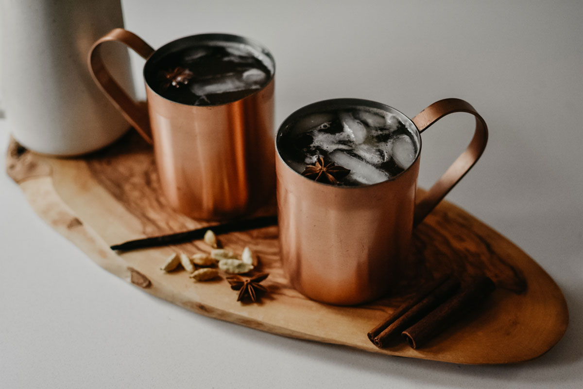 chai-spiced apple cider in copper mugs on a wooden cutting board