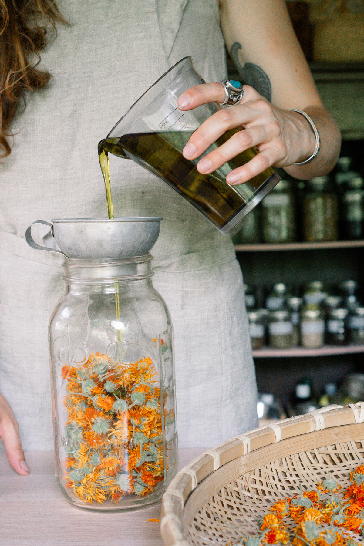 A woman pouring oil into a jar of vibrant calendula flowers
