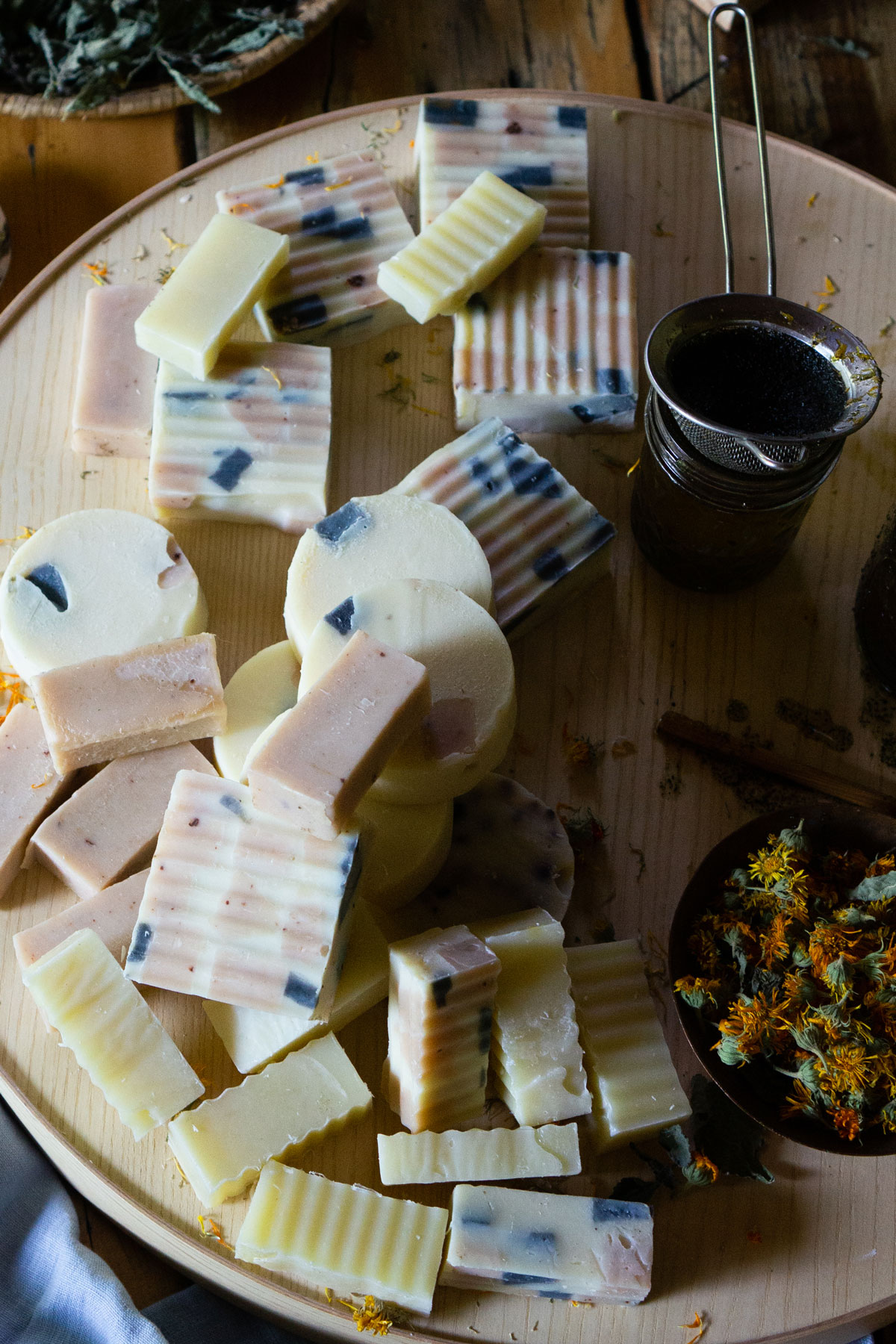 Homemade soaps, oils, and flowers scattered on a wooden tray