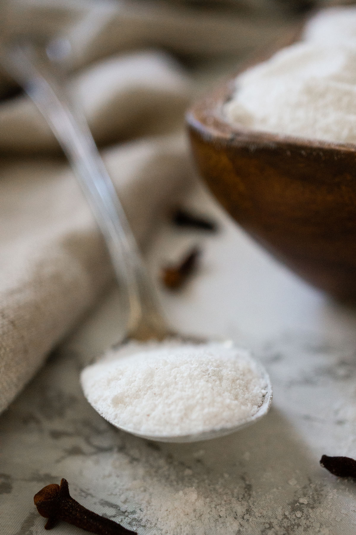 spoon of sugar with a wooden bowl of sugar in background