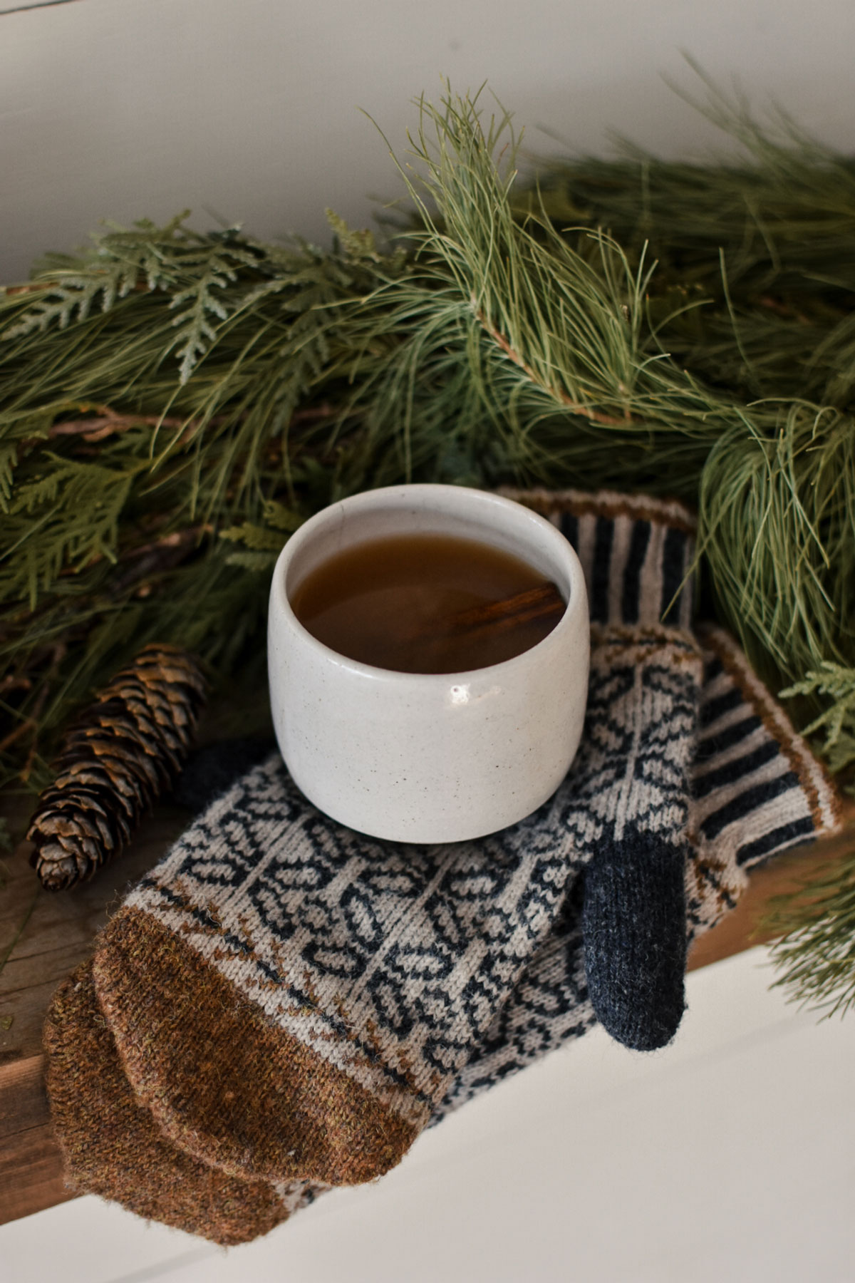 Spiced apple cider in a mug sitting on top of a pair of cozy mittens