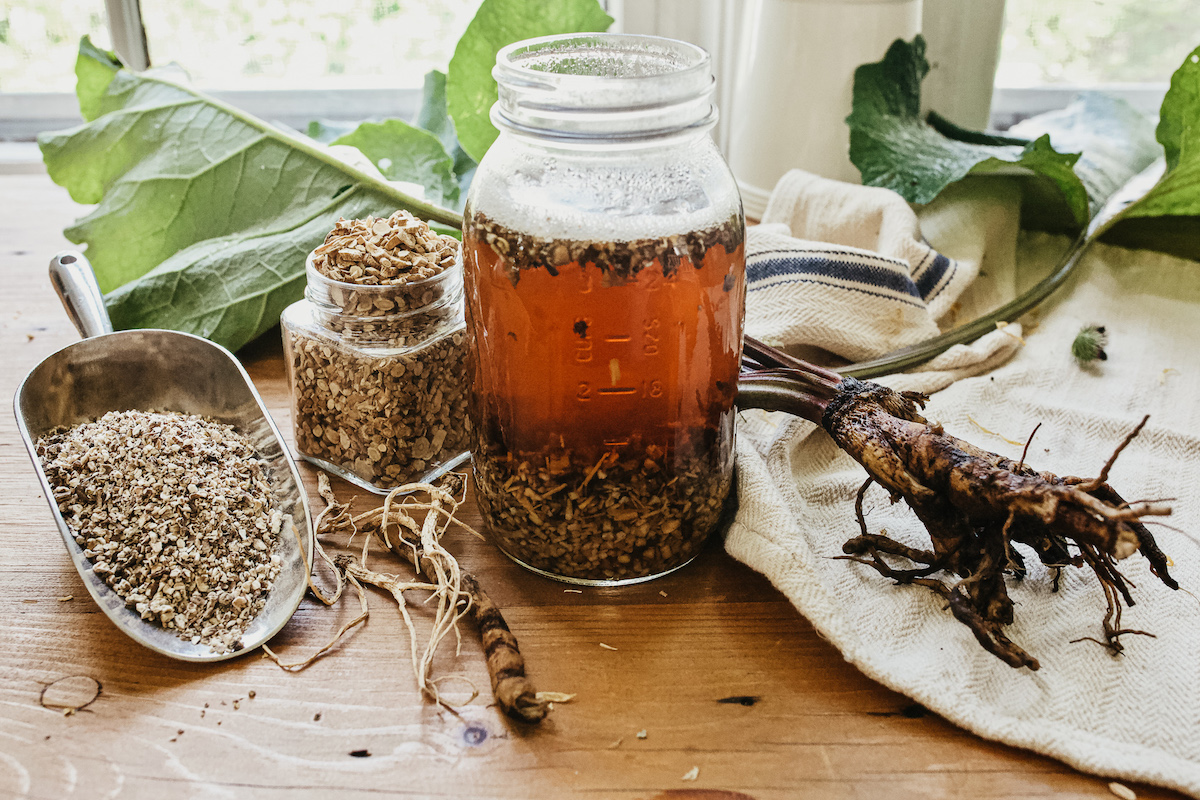 jar of decoction with dried herbs on table next to it