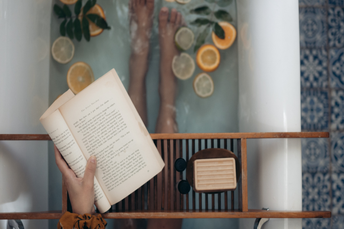 woman reading a book while in the bathtub with floating lemon and orange slices in the water: a relaxing way to boost immunity