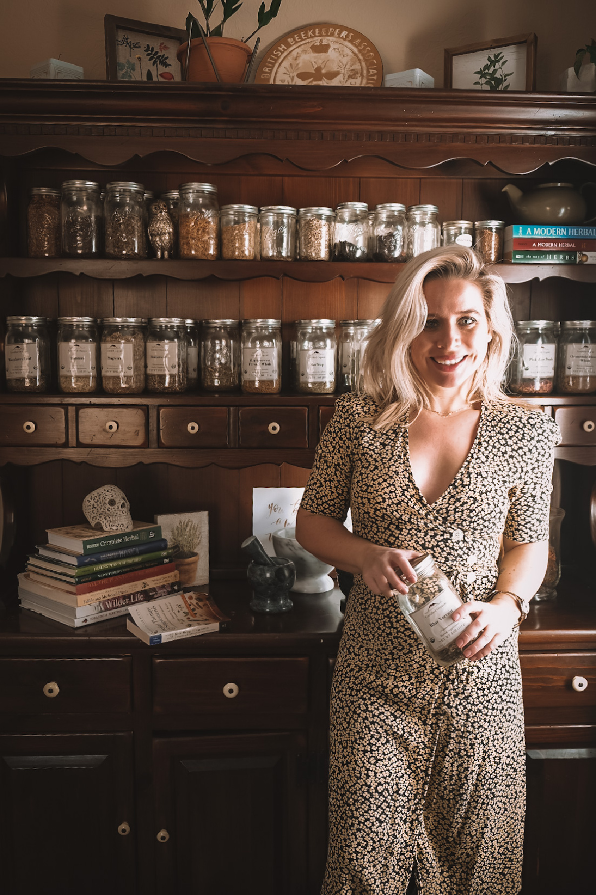 herbalist Caitlin Frazier standing in front of a shelf full of herbs and herbal books