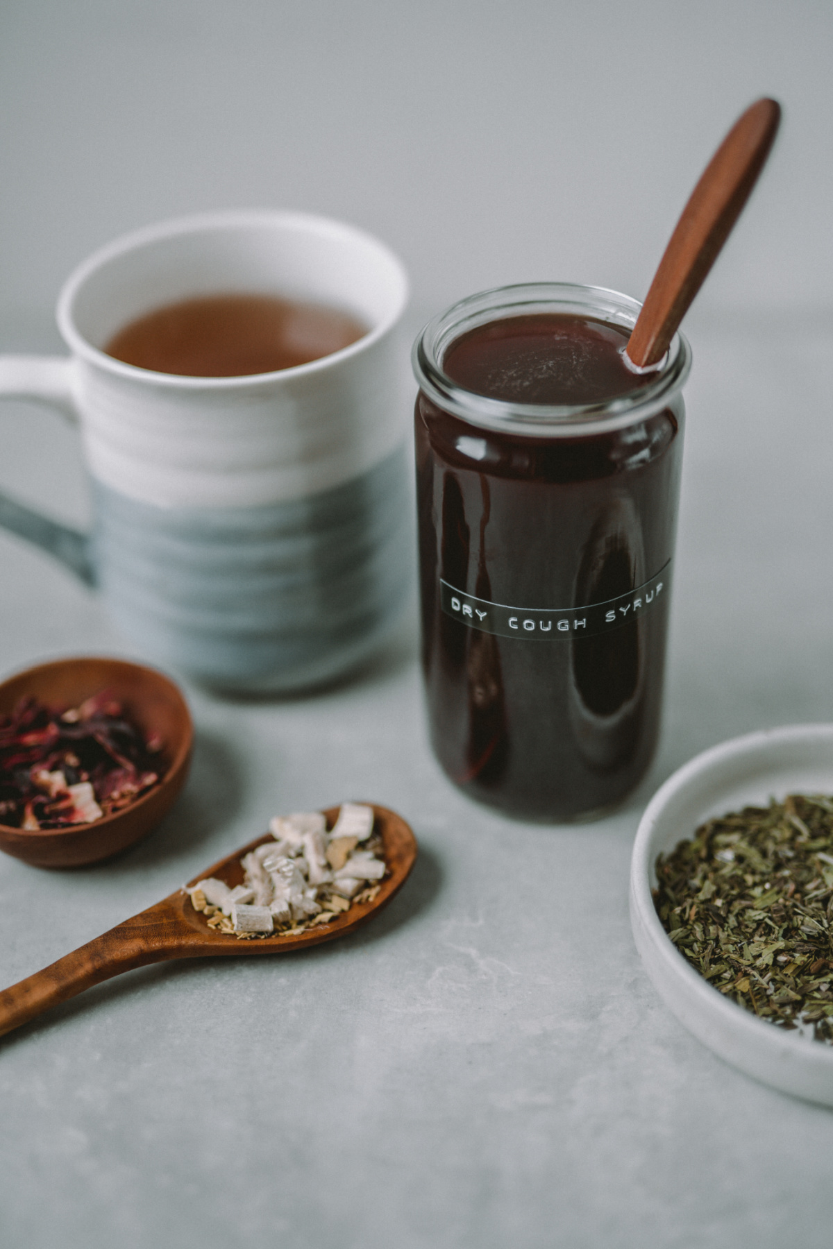 dry cough syrup recipe in a jar with dried herbs on table 