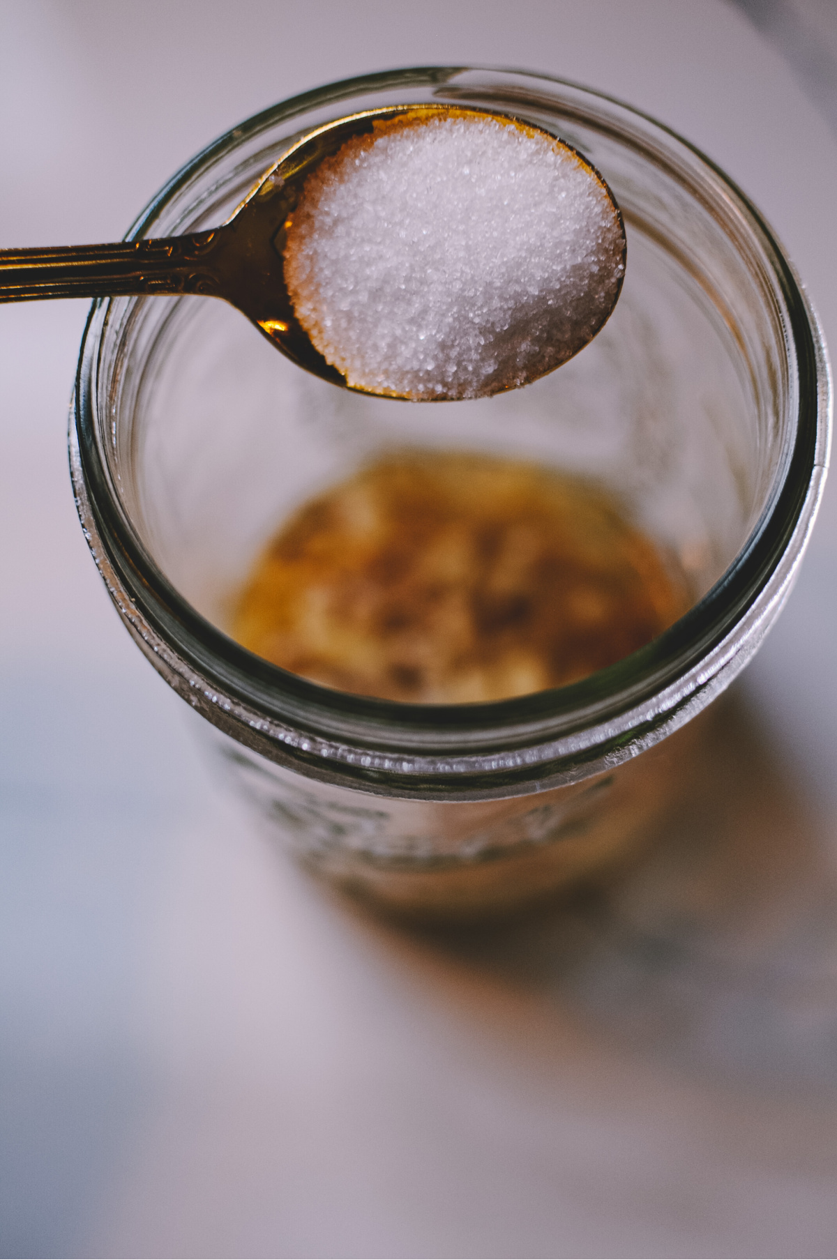 sugar on a spoon ready to be poured in the jar of ginger water to make a ginger bug