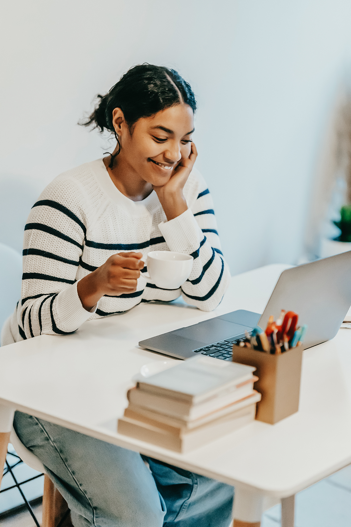smiling woman holding a white mug while looking at a laptop