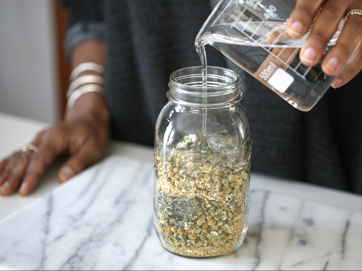 pouring glycerin into a jar of herbs
