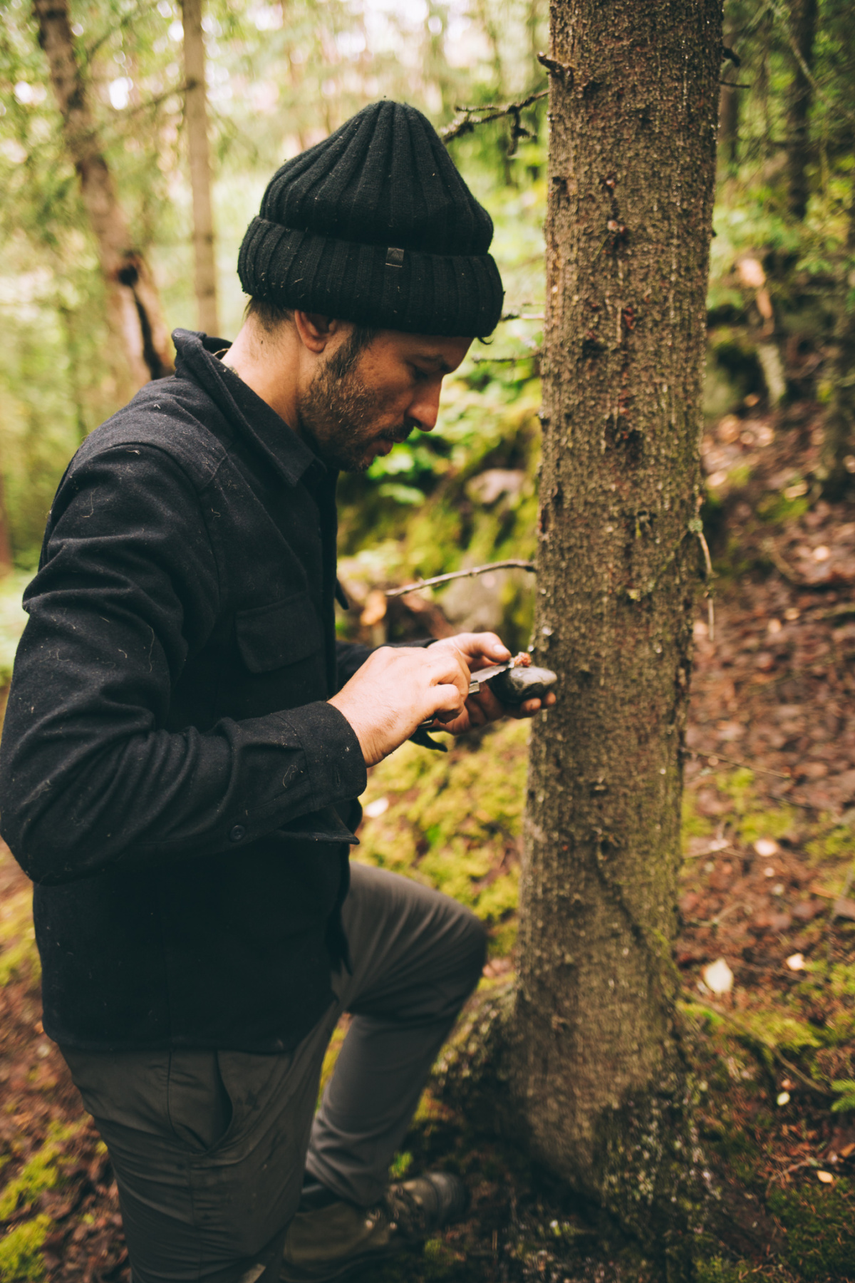 man standing by a tree holding a knife and rock