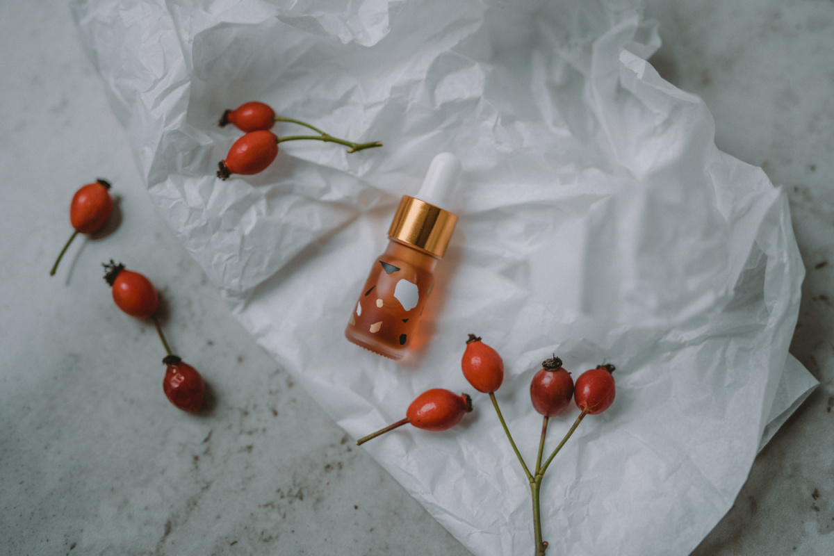 bottle of rosehip syrup and fresh rosehips on a table 