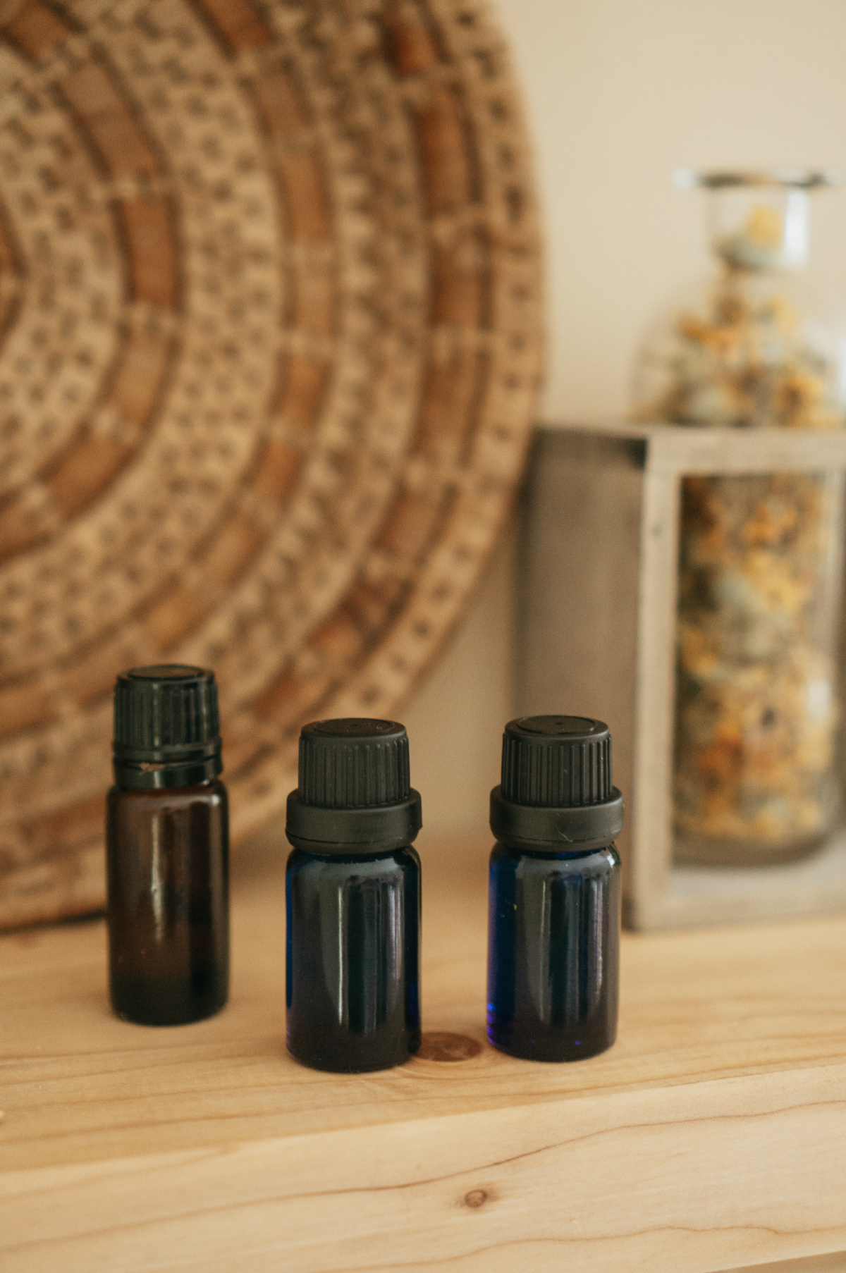 three essential oil bottles on a table with a basket and bottle of dried herbs in the background.