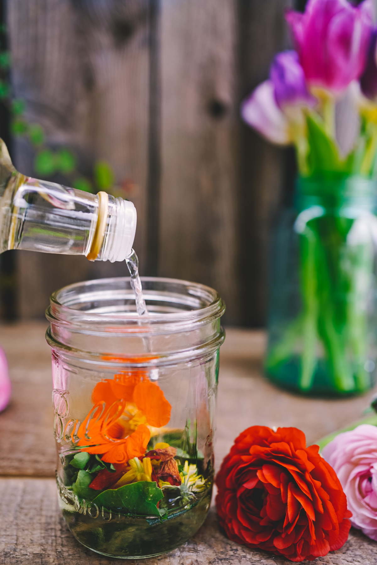 pouring white vinegar over flowers in a jar