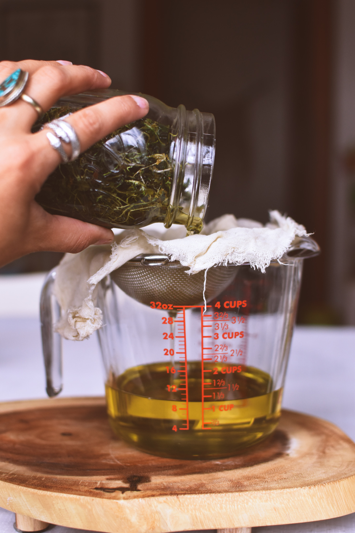 straining chickweed oil into glass measuring cup