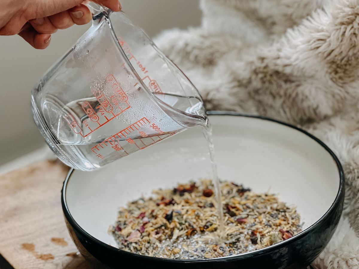 pouring water into a bowl of dried herbs for an herbal steam