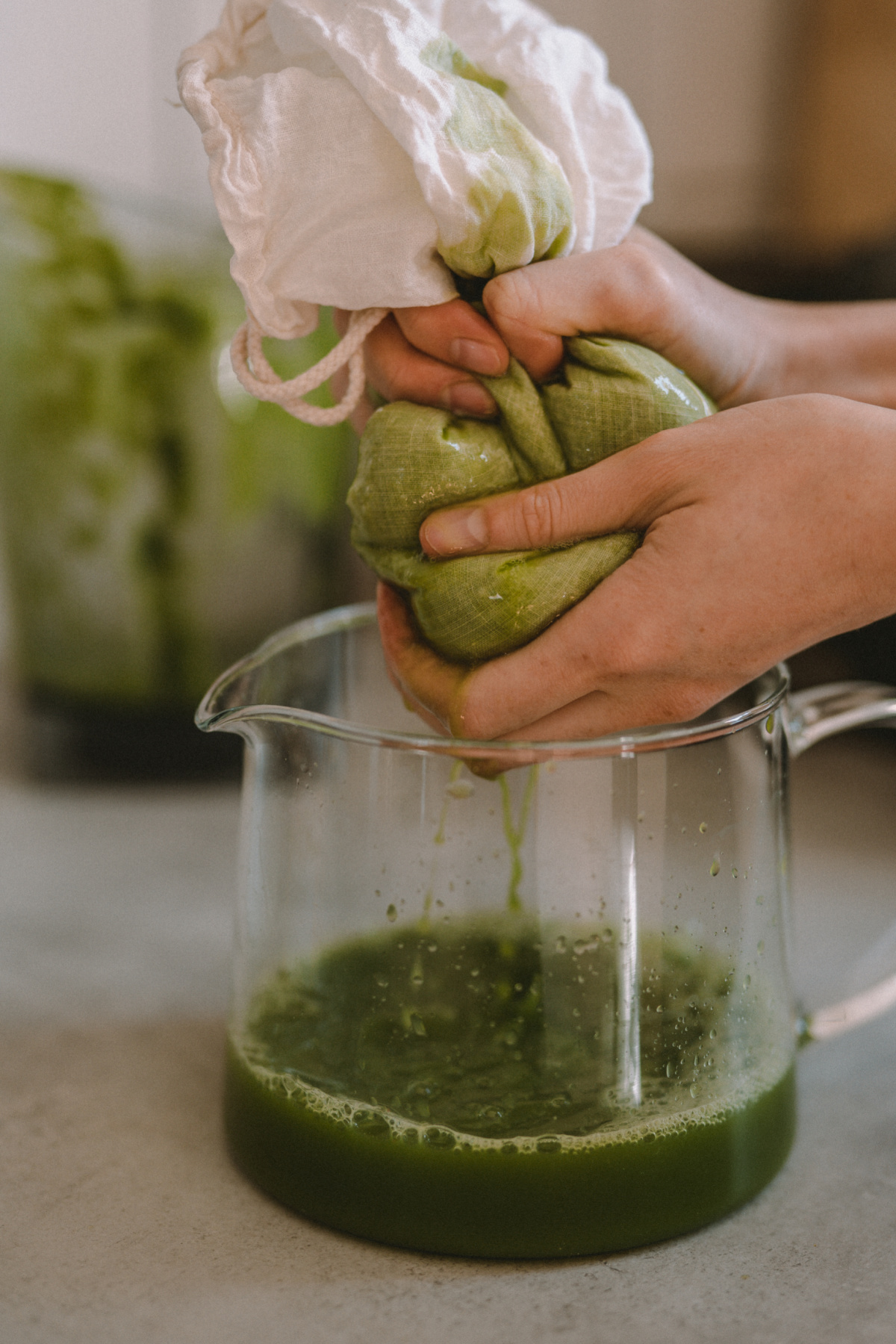 squeezing a cheesecloth of green juice into a measuring jar