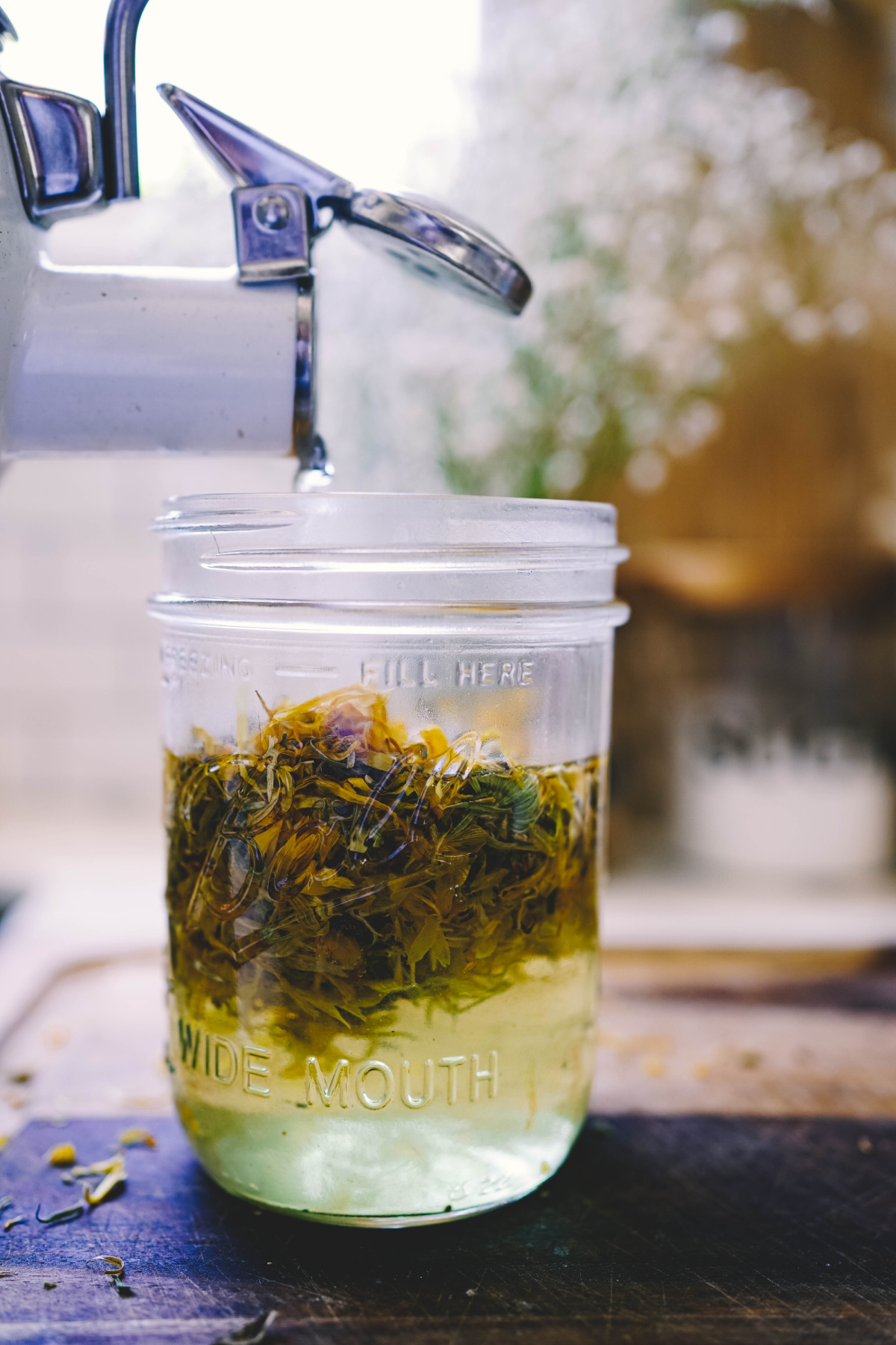 tea kettle pouring water into a jar of calendula