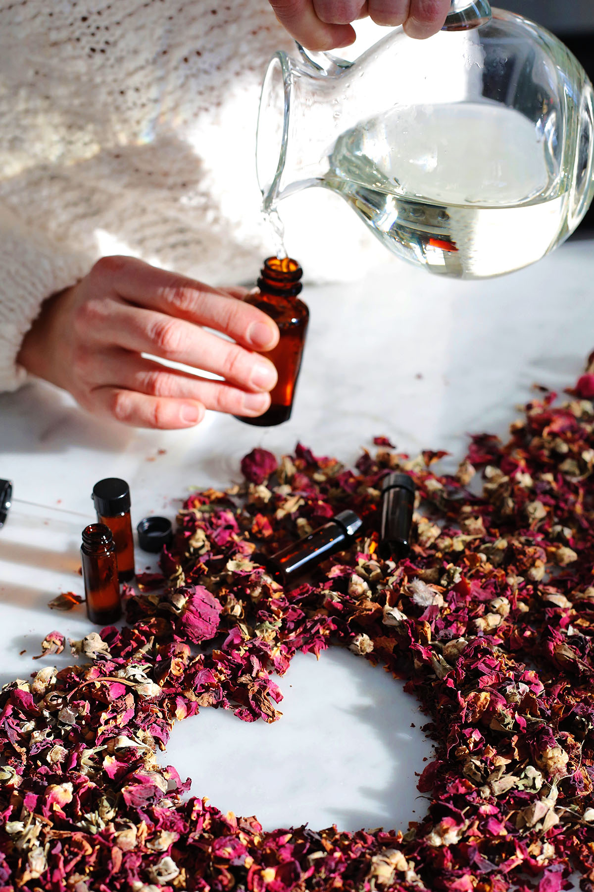 water being poured into an amber glass bottle with rose petals on a table 