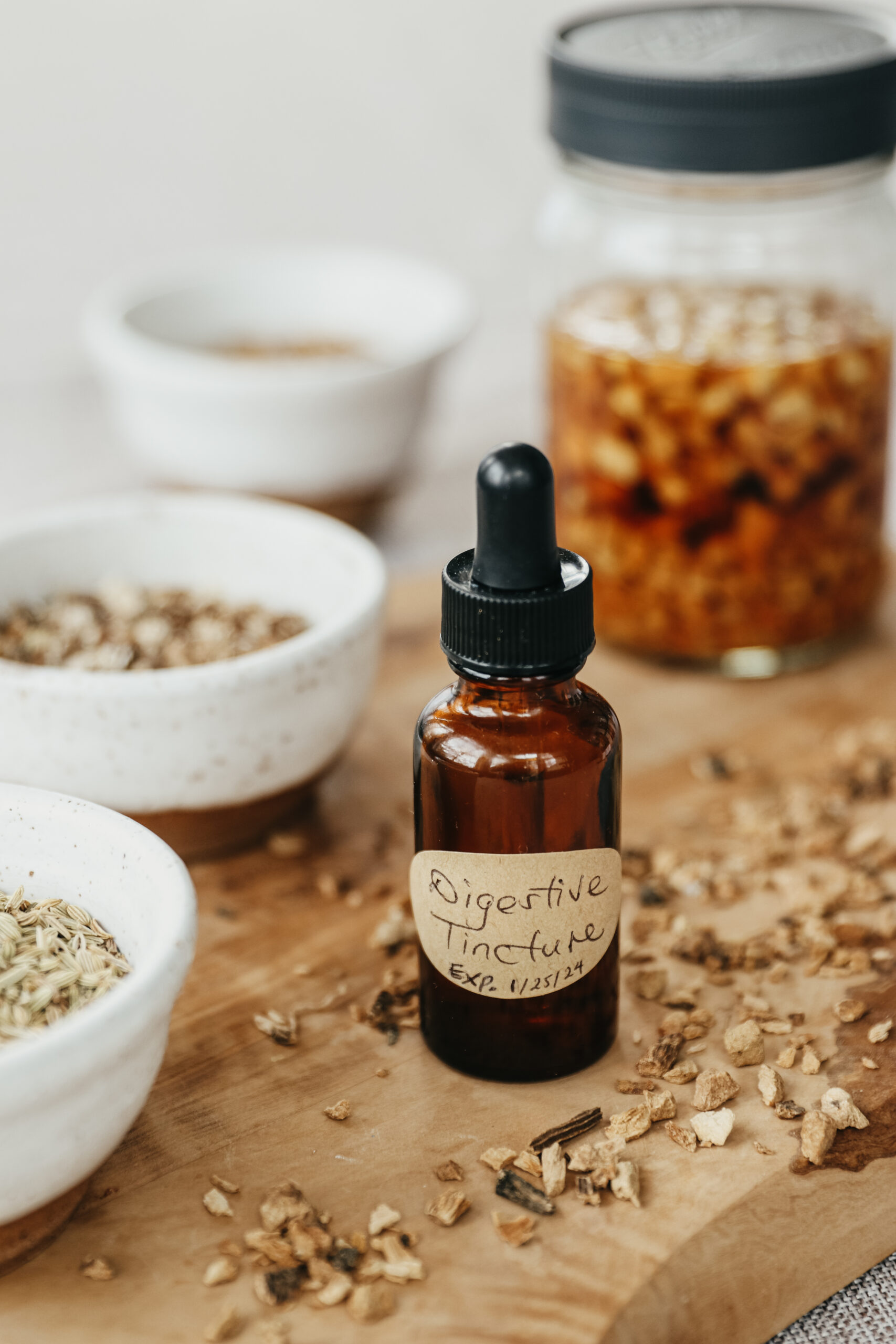 bottle of digestive tincture with bowls of dried herbs on a wooden board and a jar of tincture in the background