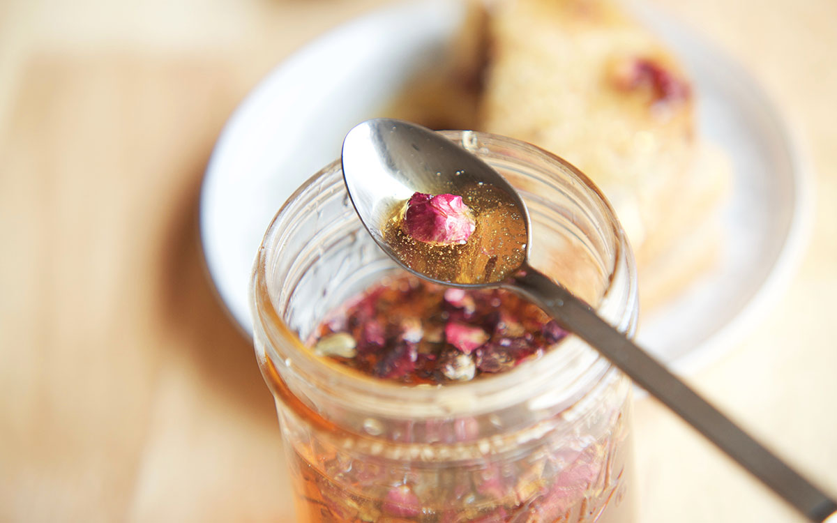 rose infused honey in a jar with honey and a rose petal on a spoon