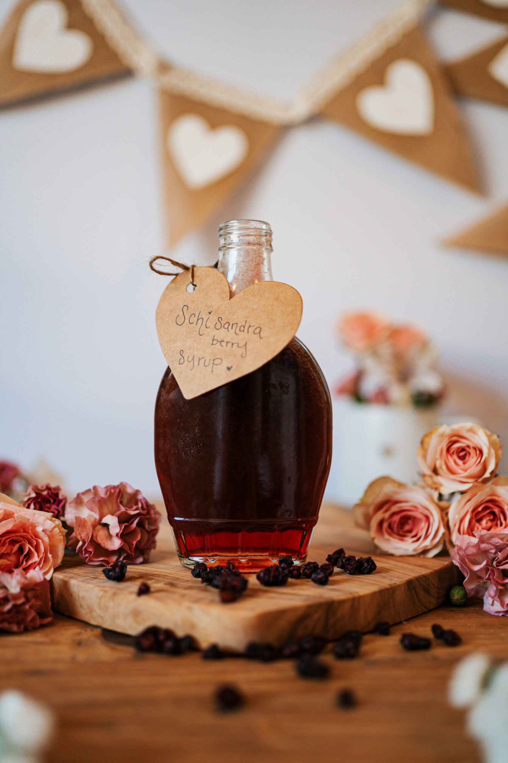 schisandra berry syrup in a glass bottle sitting on a wooden board with roses and a Valentine's Day banner hanging in the background