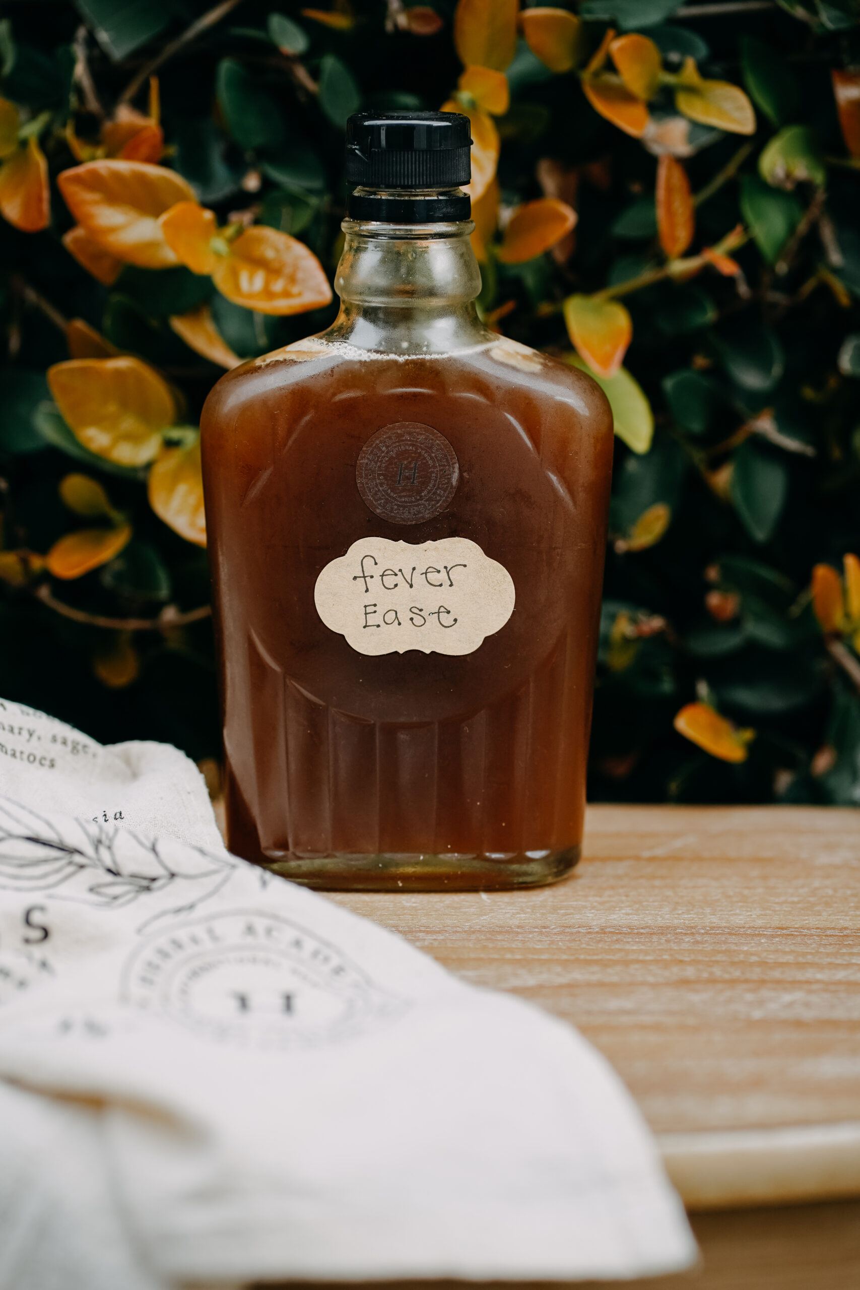 bottle of herbal fever ease sitting on table with a plant in the background and towel laying next to it