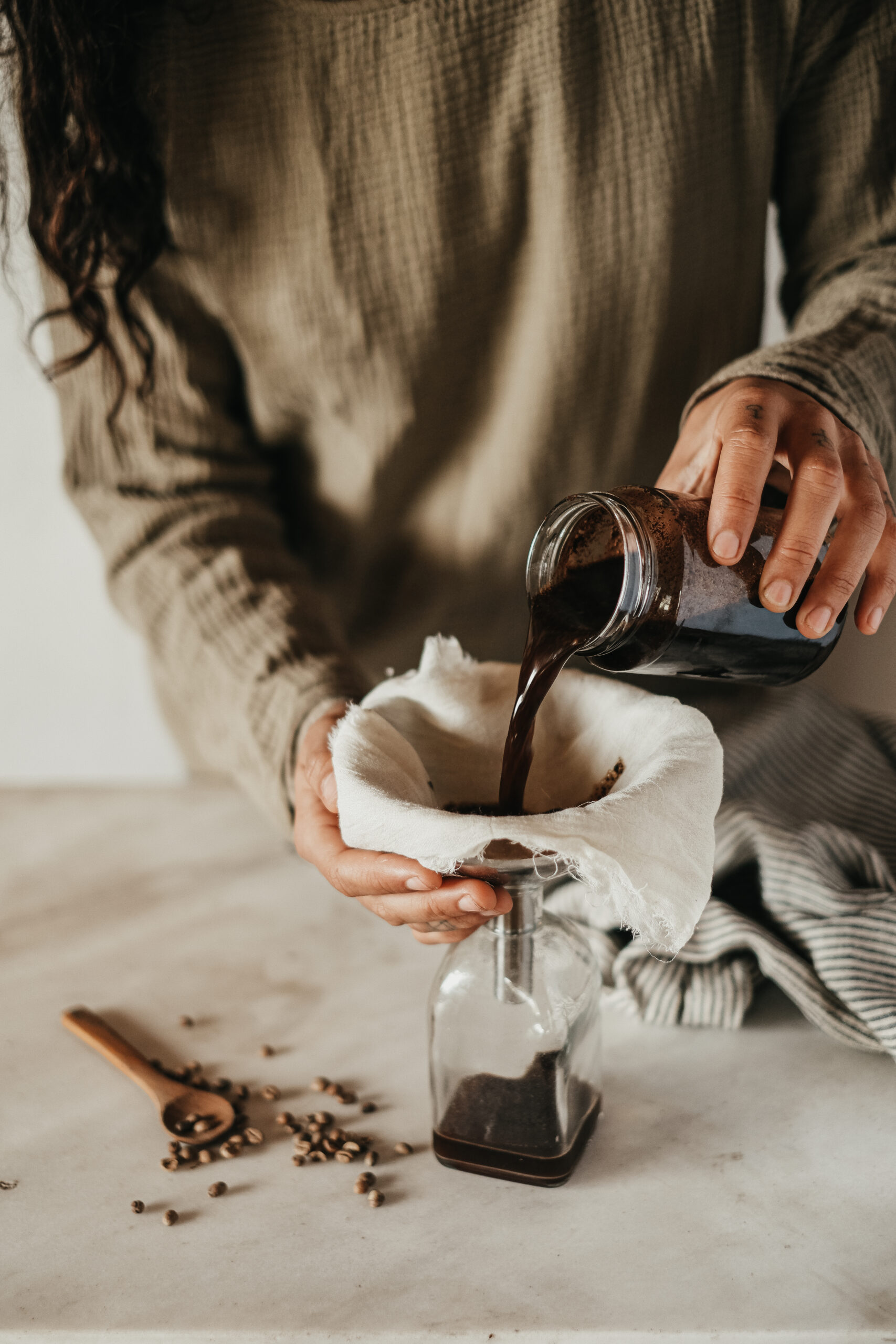 woman pouring coffee extract through a cheesecloth and funnel