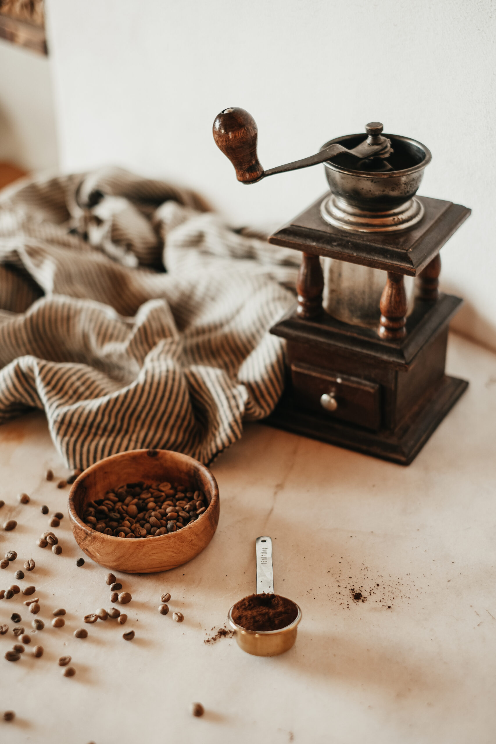 photo of coffee grinder, wooden bowl of coffee beans, and ground coffee in a small measuring cup
