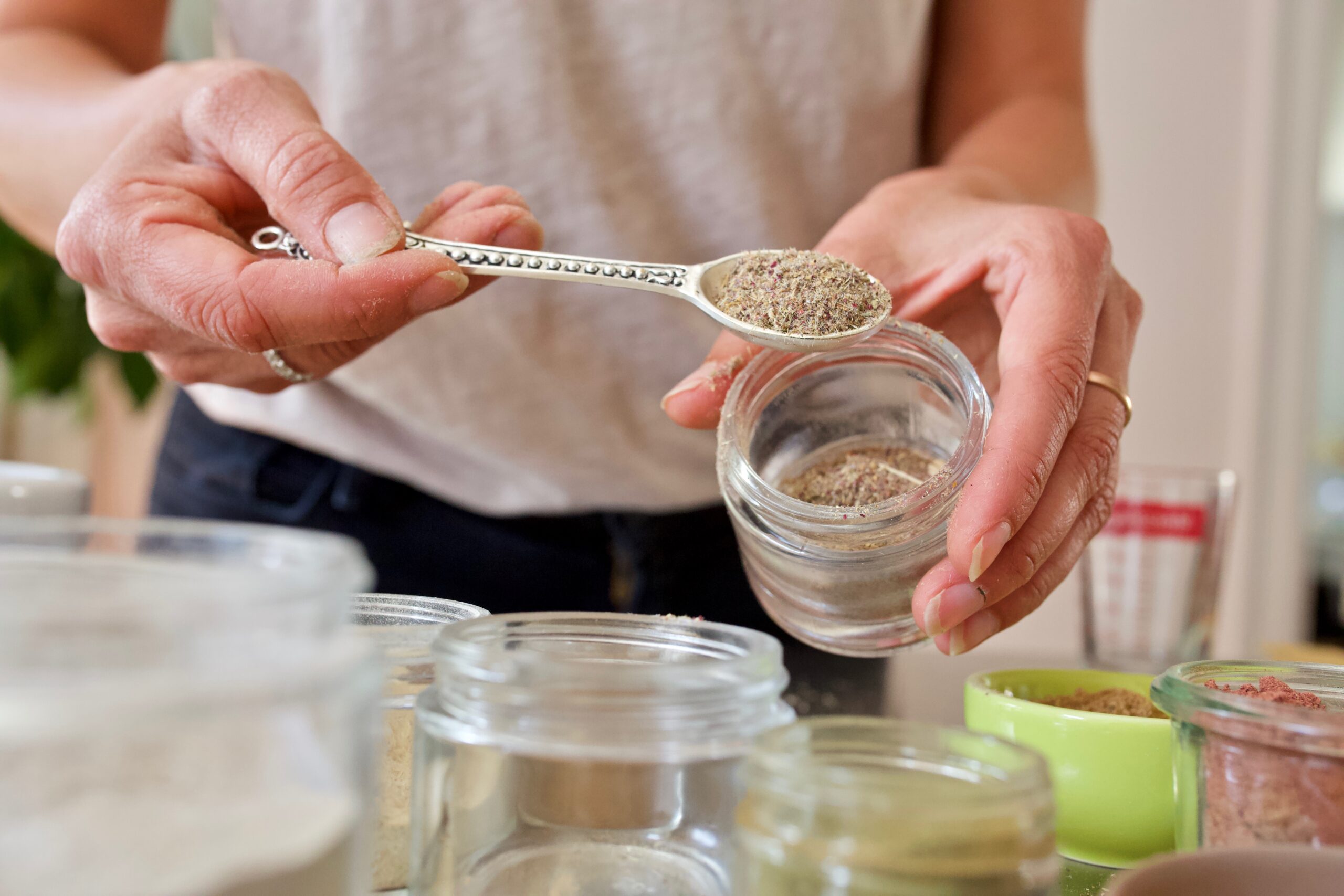 woman with a spoon of dried herbs from a glass jar