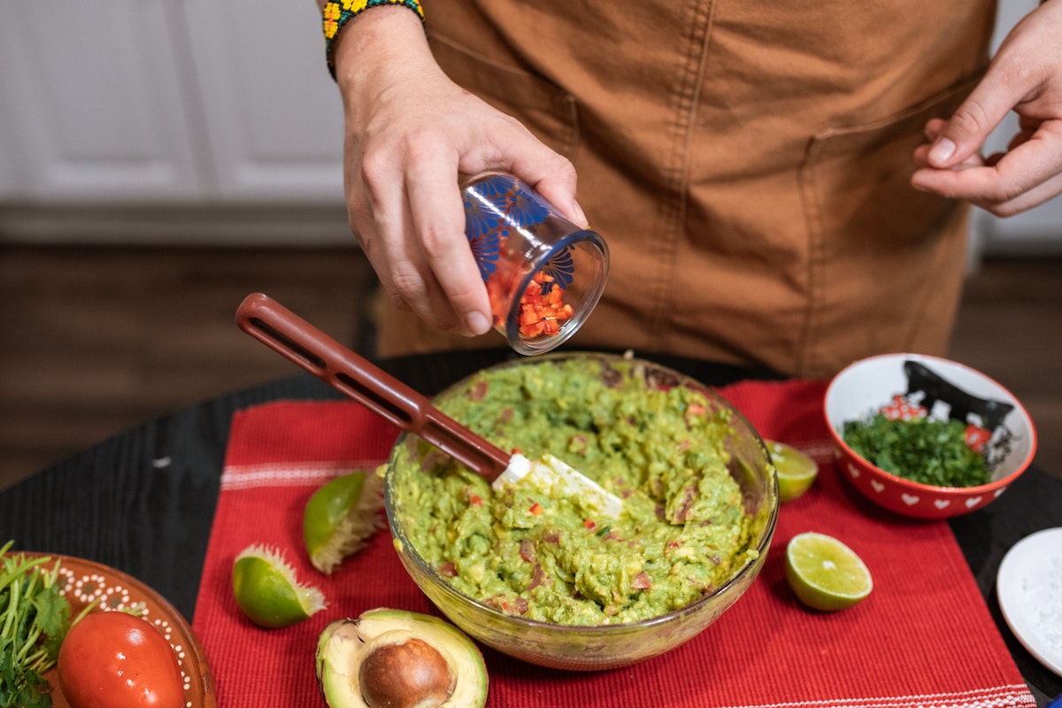 pouring tomatoes into a bowl of guacamole