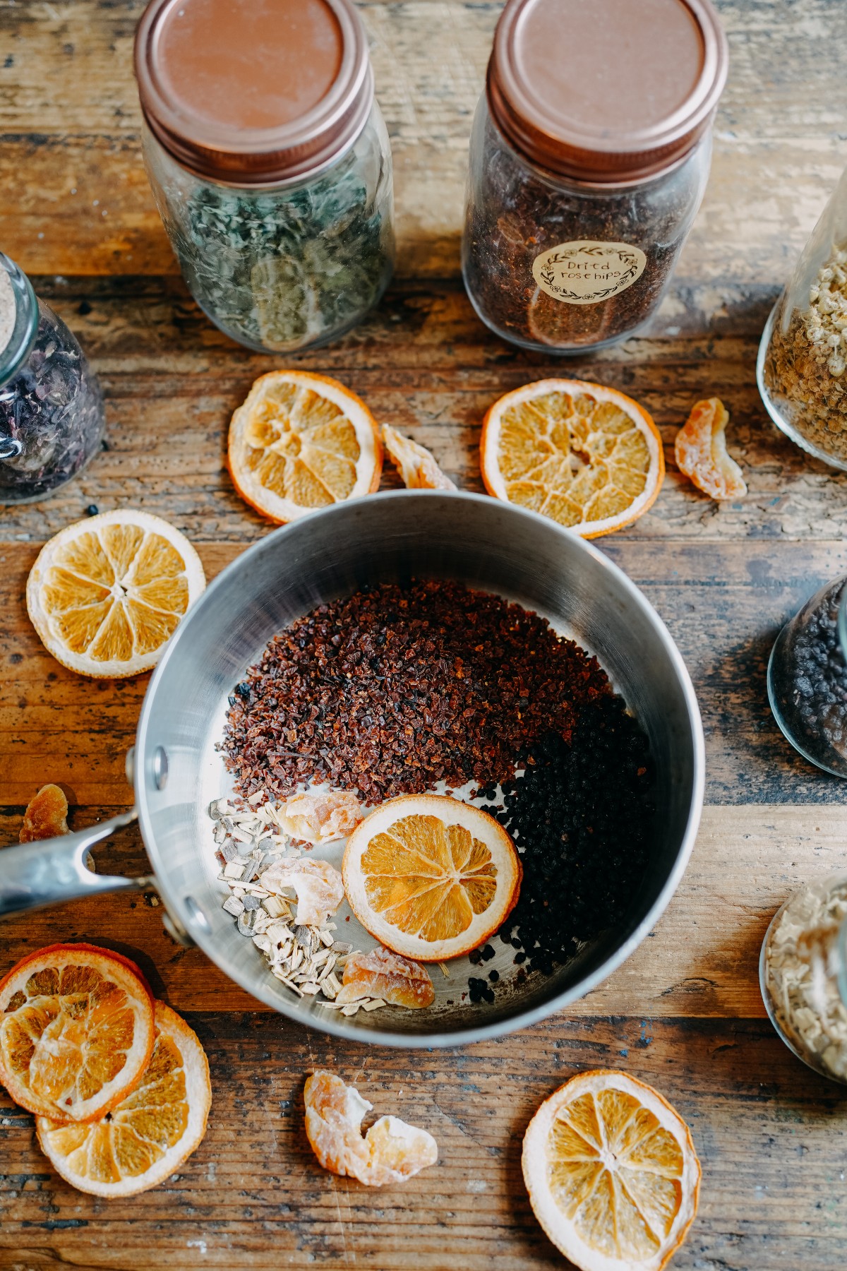 saucepan with herbs in the bottom and surrounding pan with jars of herbs on a wooden table 