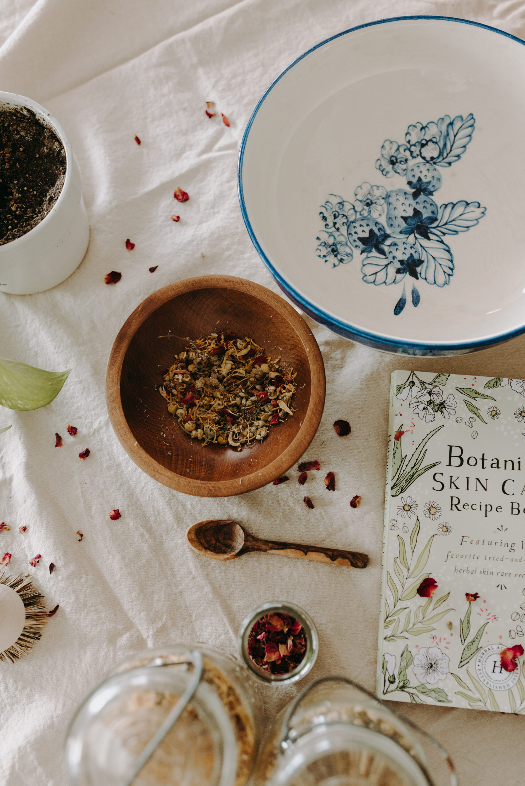 bowls of herbs and Botanical Skin Care Recipe book on a tablecloth