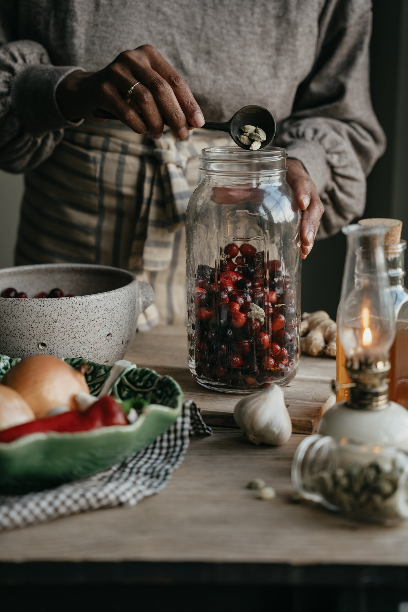 herbalist pouring cardamom seeds into a jar of cranberries