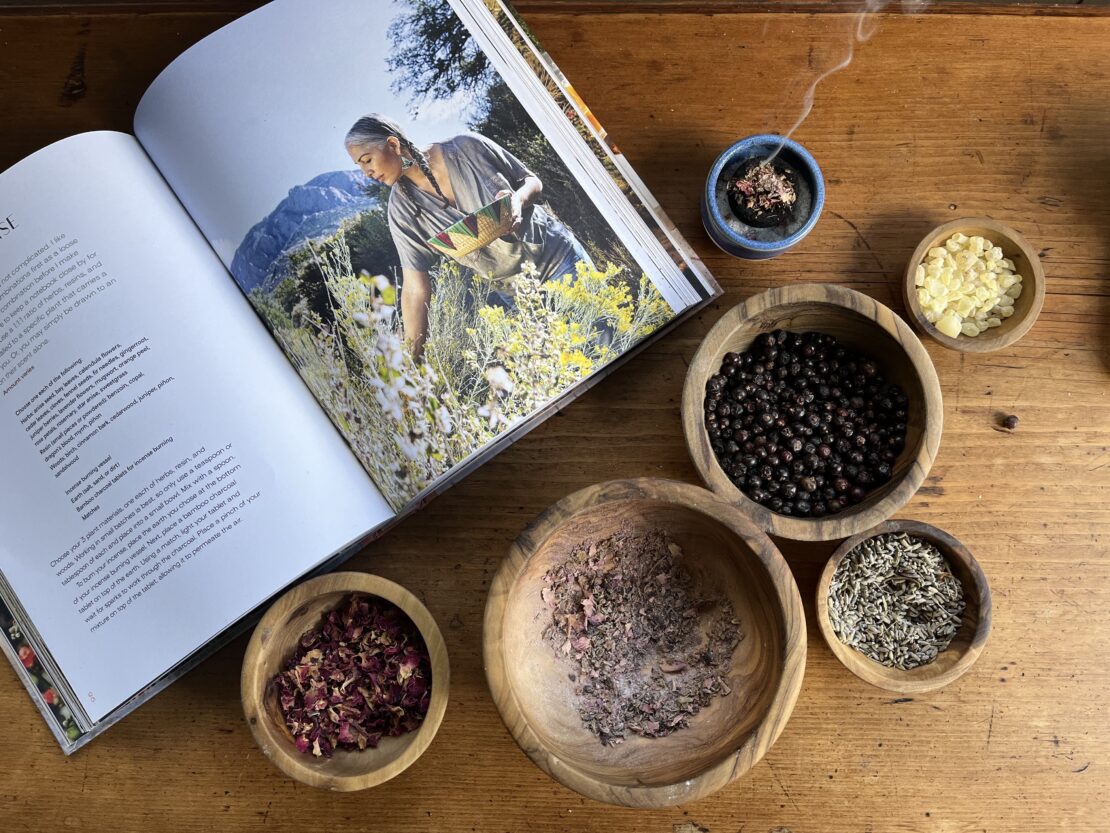 Earth Medicines book open on a table with wooden bowls of herbs