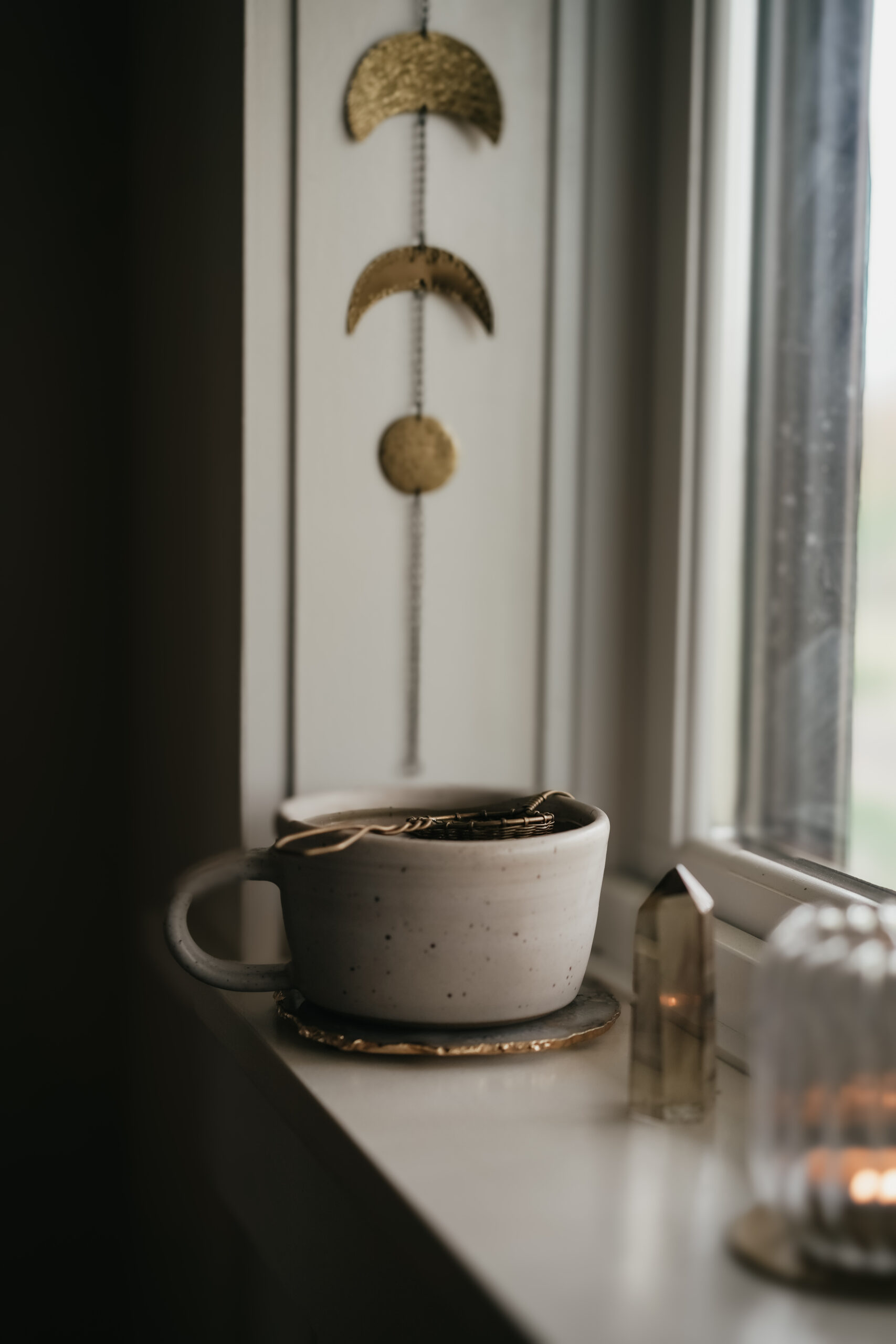 herbal infusion sitting in a windowsill with a chain of moon phases in the background