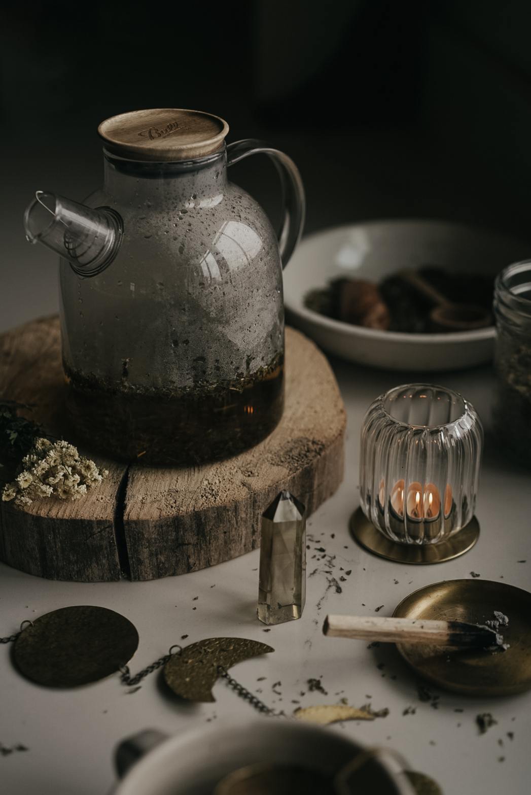 herbal infusion sitting on a wooden stump with a burning candle and moon phases on a chain on the table next to it