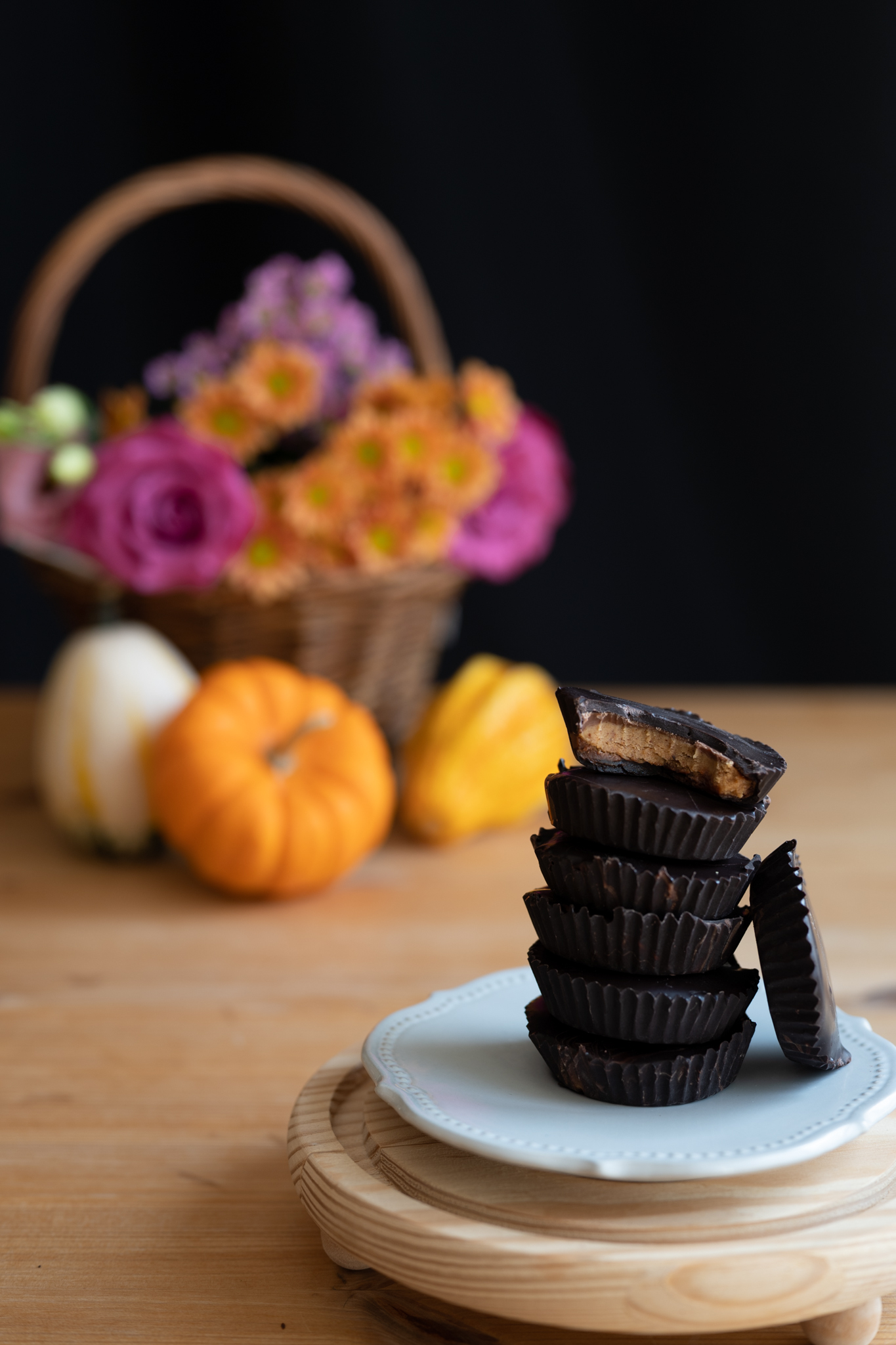 a stack of herbal peanut butter cups on a white plate with a basket of flowers and pumpkins in the background