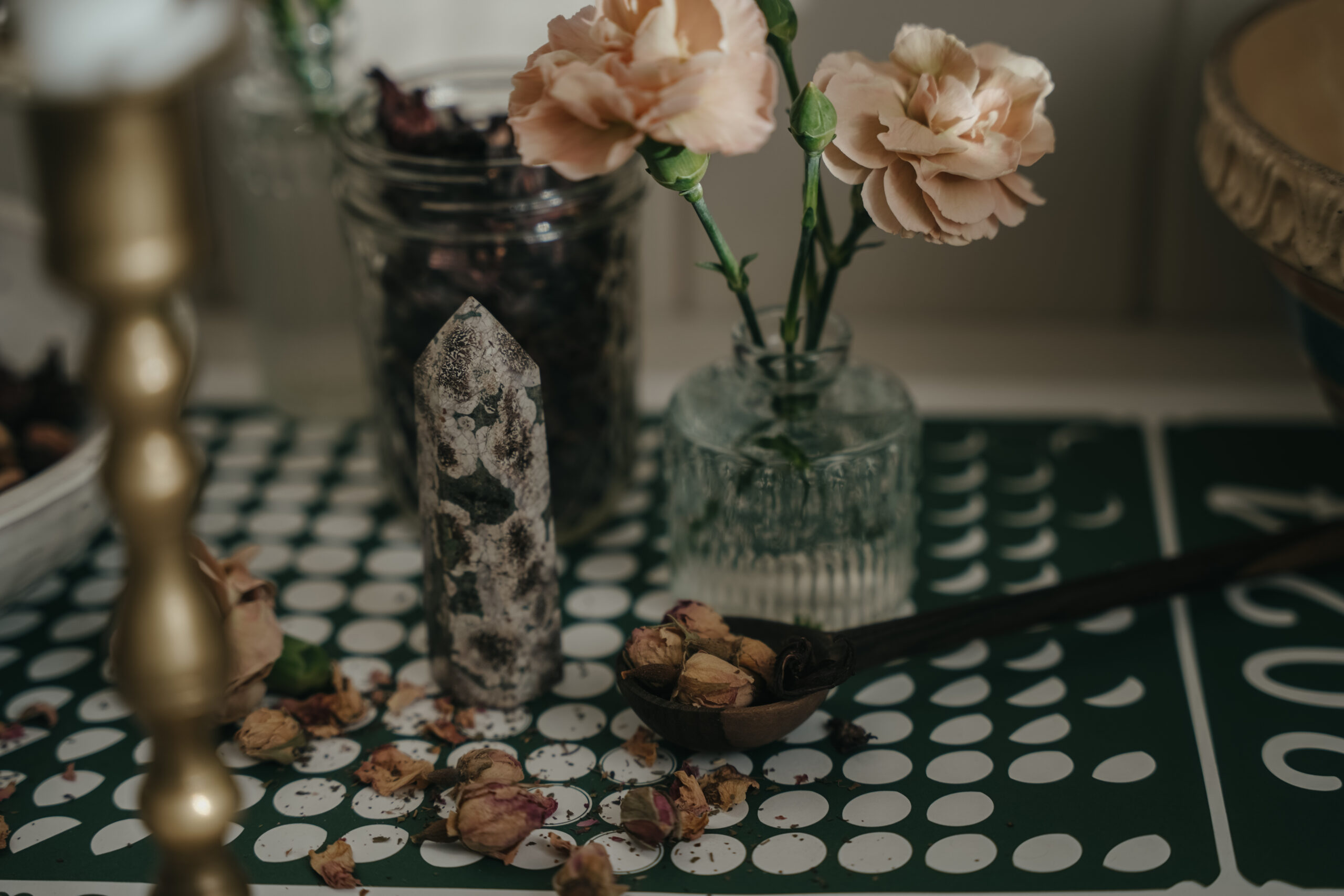 rose buds on a spoon and sprinkled on a moon calendar with vase and jar of flowers in the background