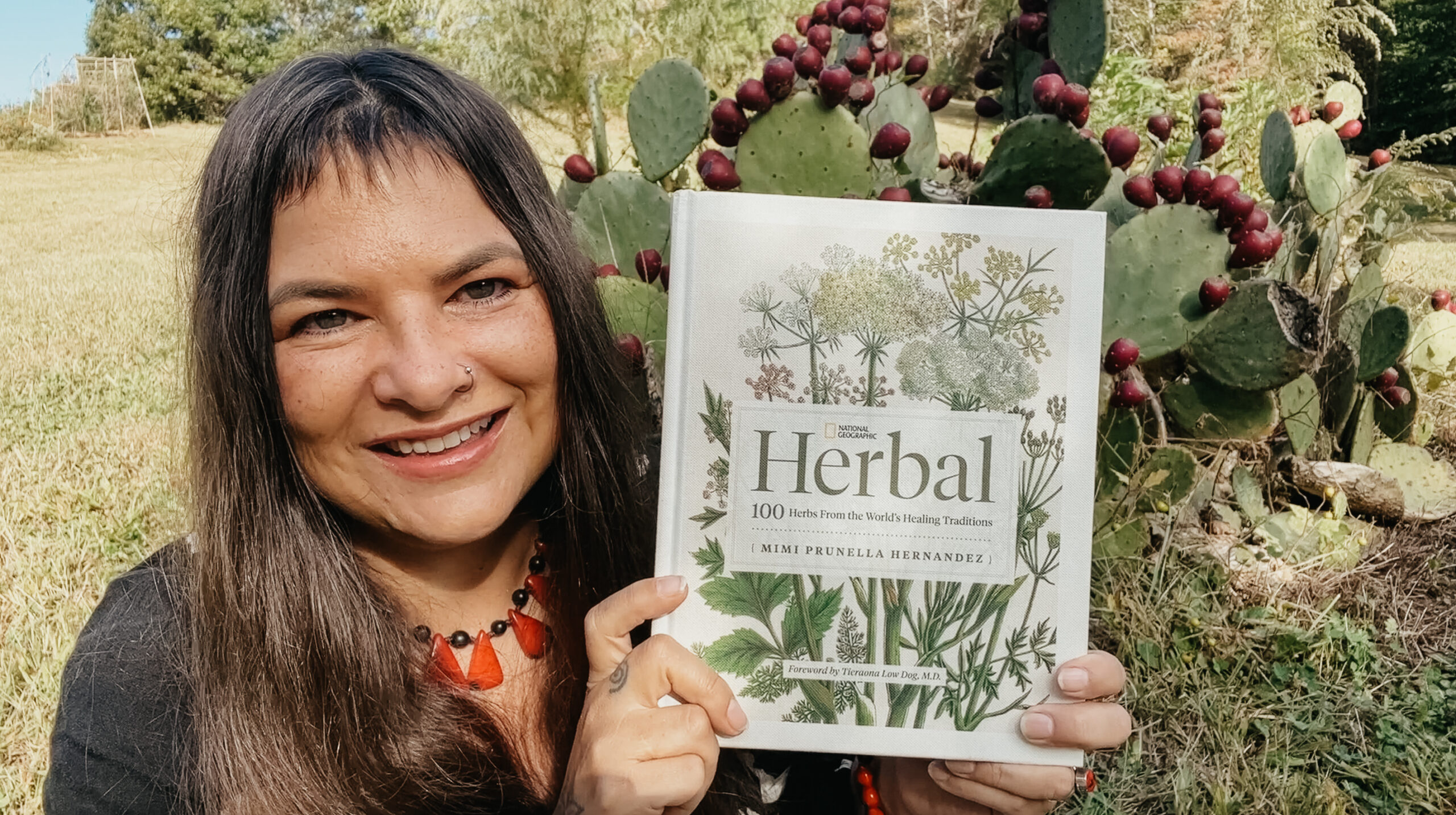 Mimi Hernandez holding the National Geographic Herbal book with a cactus in the background